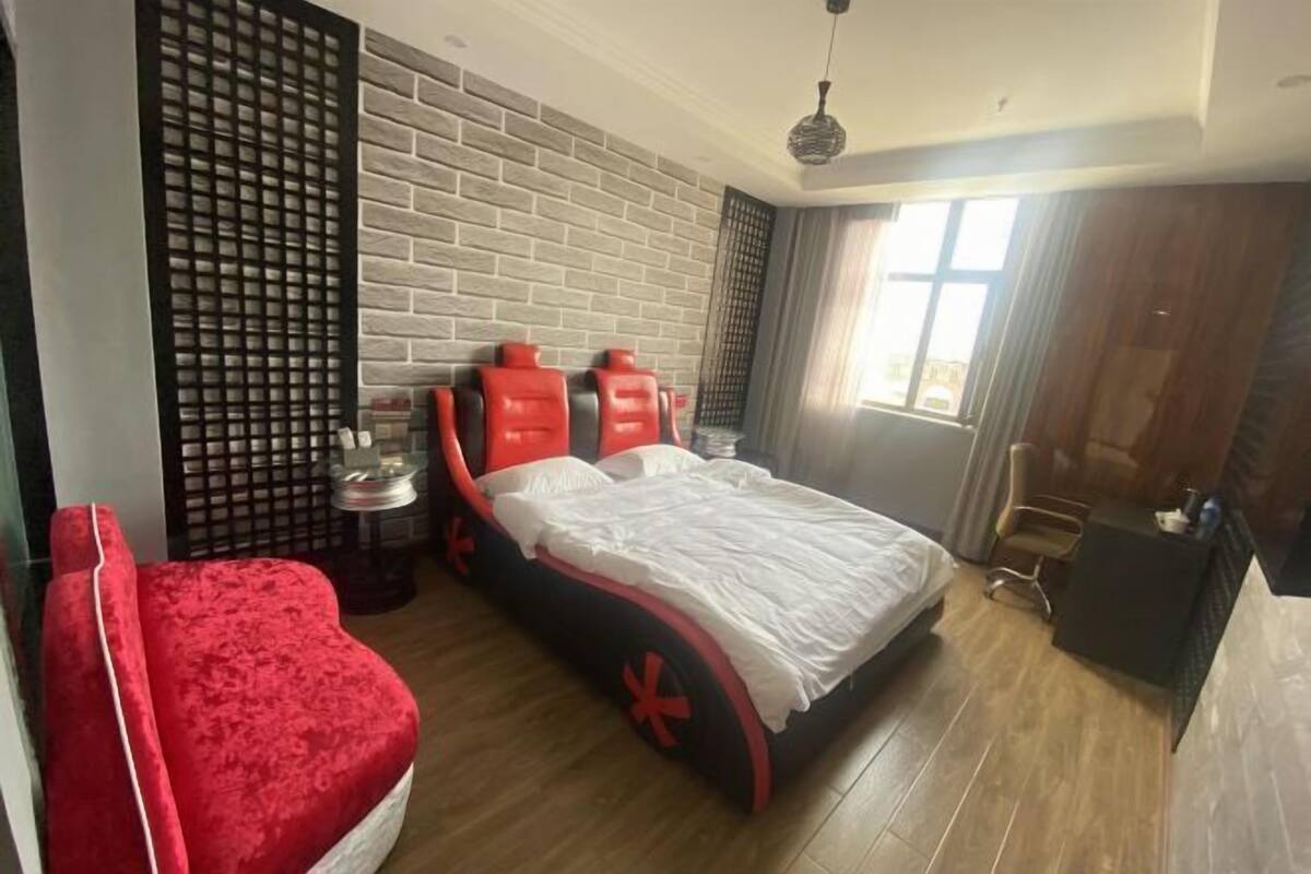 Une chambre d’hôtel avec un lit, une chaise rouge, un bureau et une fenêtre.