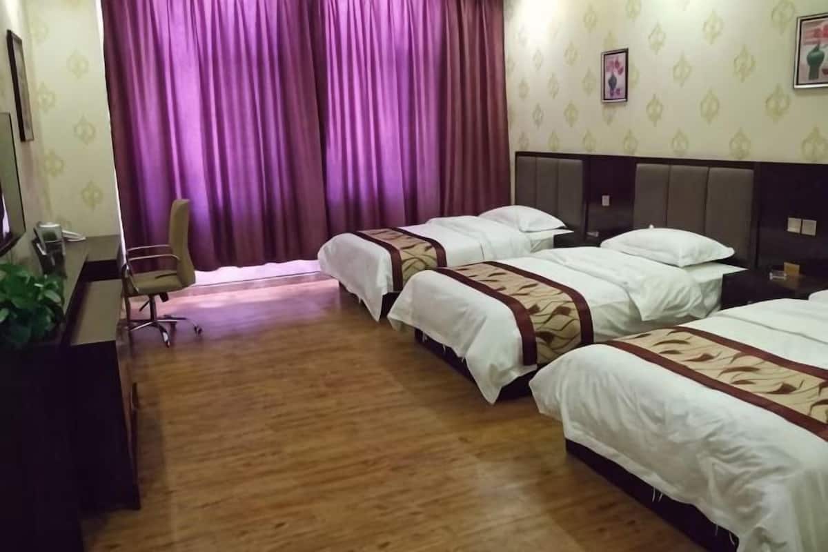 Une chambre d’hôtel avec trois lits, un bureau, une chaise et une grande fenêtre avec des rideaux violets.