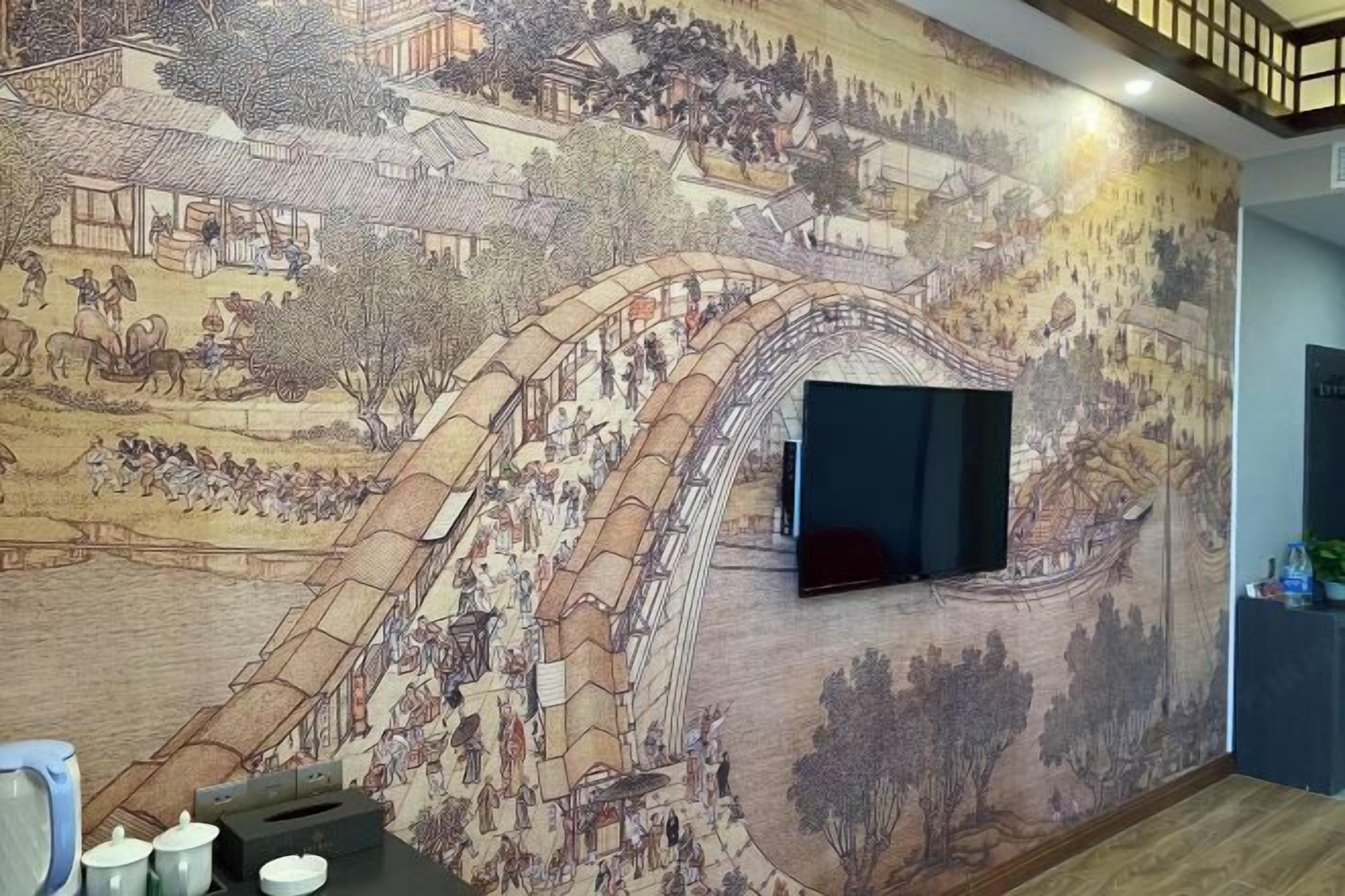 Una habitación con un amplio mural que representa una escena histórica, un televisor de pantalla plana montado en la pared y una pequeña mesa con algunos objetos encima.