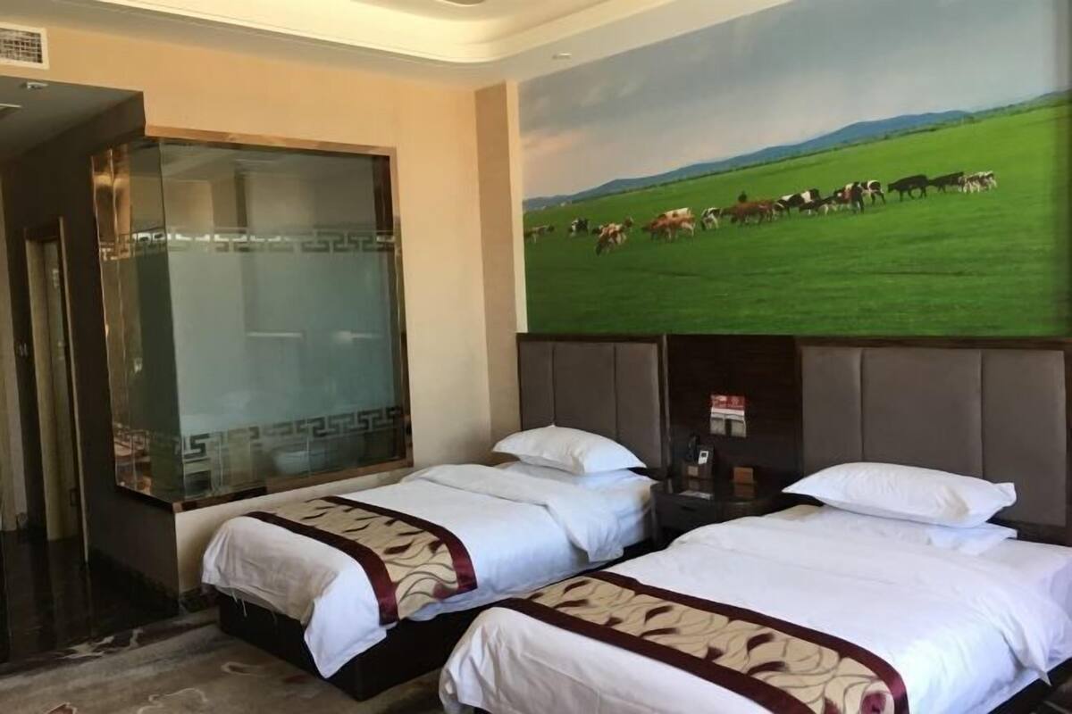 Une chambre d’hôtel avec deux lits, une grande fenêtre et un tableau représentant un champ avec des vaches.