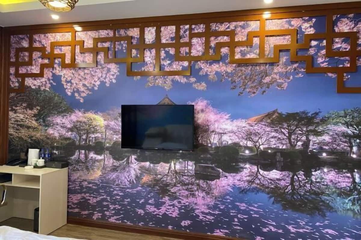 Une pièce avec un téléviseur fixé au mur, orné d’une fresque représentant des fleurs de cerisier, un bureau avec une chaise et un lit.