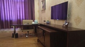 A hotel room with a wooden desk, a chair, a television, and a small table with a coffee maker. - Moli International Hotel (Erenhot)