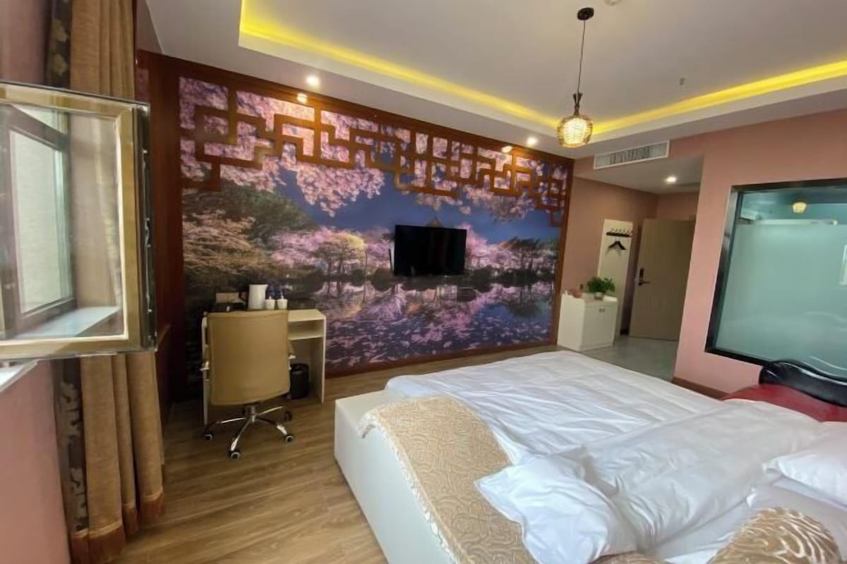 A hotel room with a bed, a desk, a chair, a television, and a decorative wall.