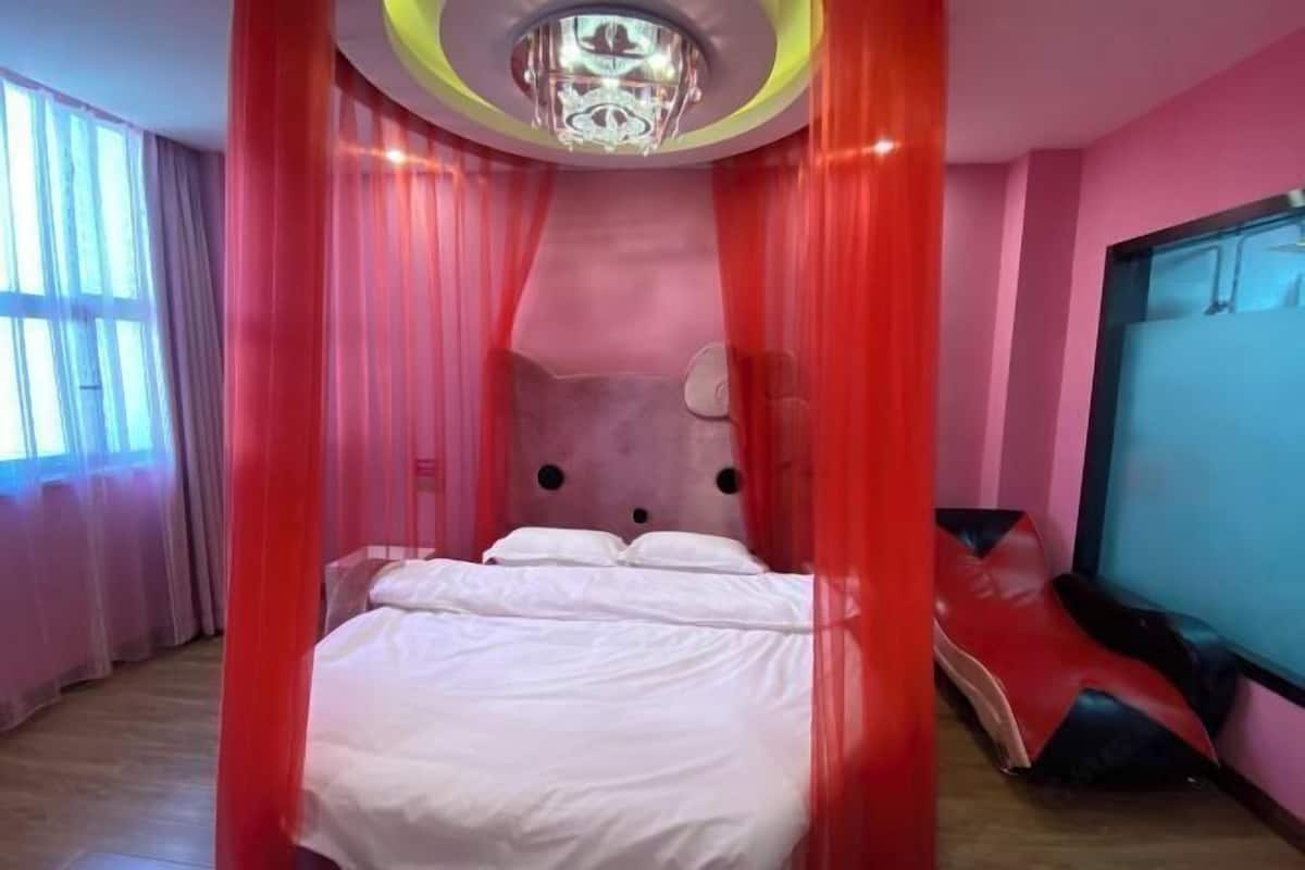 Une chambre avec un lit, un baldaquin rouge, un lustre et une fenêtre avec des rideaux.