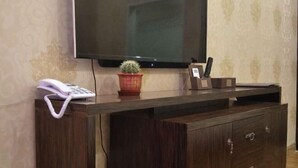 A wooden desk with a telephone, a potted plant, and a small item holder against a wall with a large flat-screen TV mounted above. - Moli International Hotel (Erenhot)