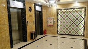 An elevator area with marble flooring, two elevators, a fire extinguisher, and a patterned door. - Moli International Hotel (Erenhot)