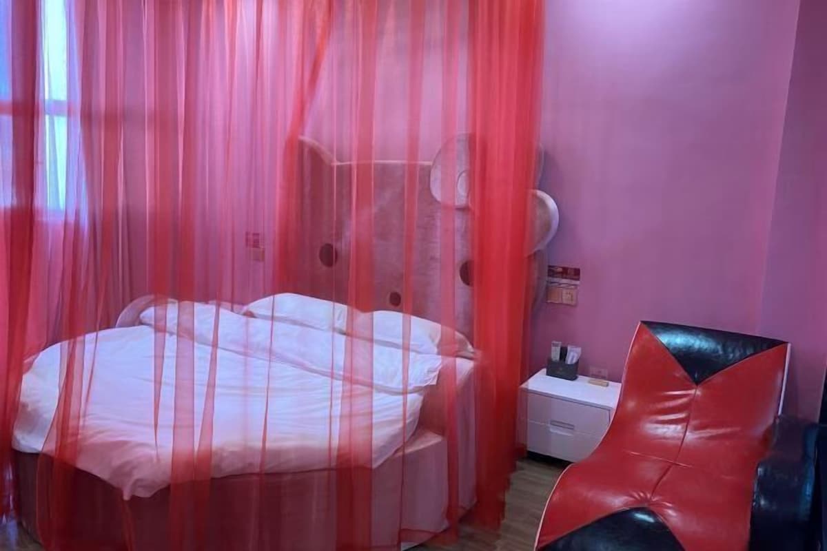 A bedroom with a bed, a nightstand, a chair, and a window with a curtain.