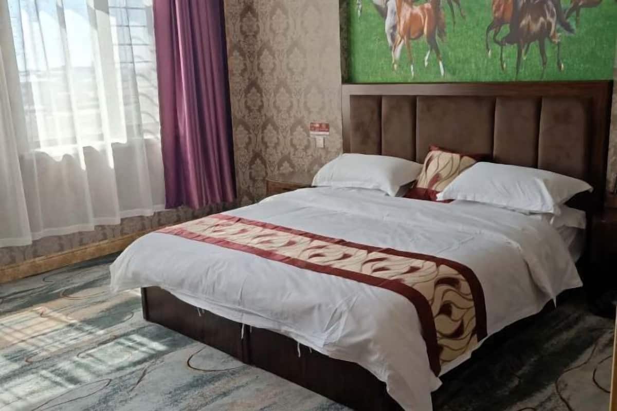 Une chambre d’hôtel avec un grand lit, une tête de lit, une fenêtre avec des rideaux et un tableau accroché au mur.