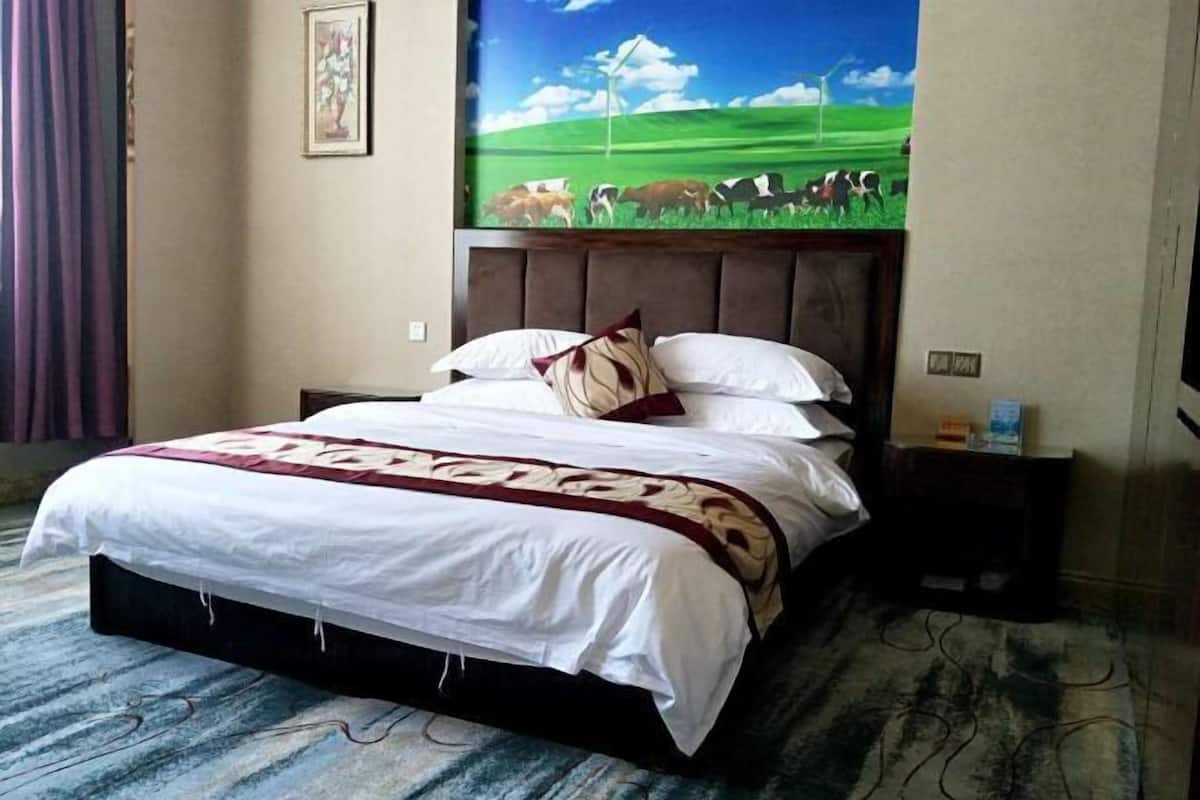 Une chambre d’hôtel avec un lit, une table de chevet, un tableau représentant des vaches accroché au mur et un rideau.