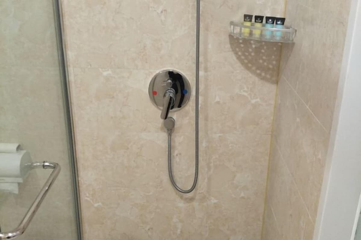 A shower with a handheld hose, a glass shower enclosure, and a shelf with toiletries.
