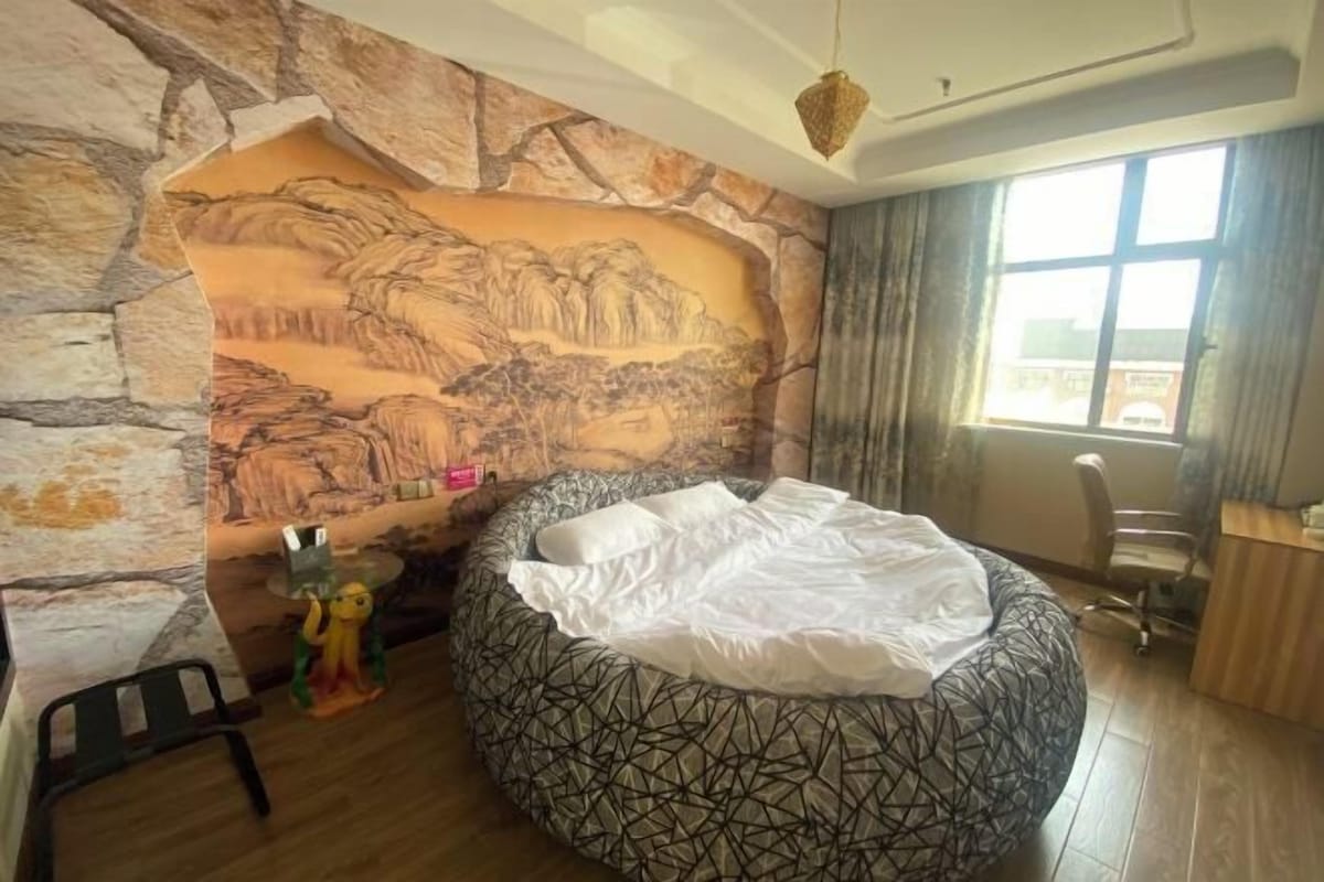 A bedroom with a round bed, a stone wall mural, a desk, and a chair.