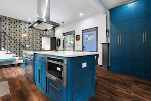 A kitchen with blue cabinets, a central island with an oven, and a staircase leading to another level.