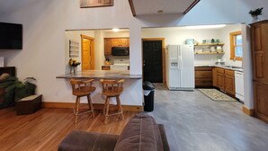 A modern kitchen with wooden cabinets, a white refrigerator, and a microwave. There is a dining area with two wooden chairs and a small table.