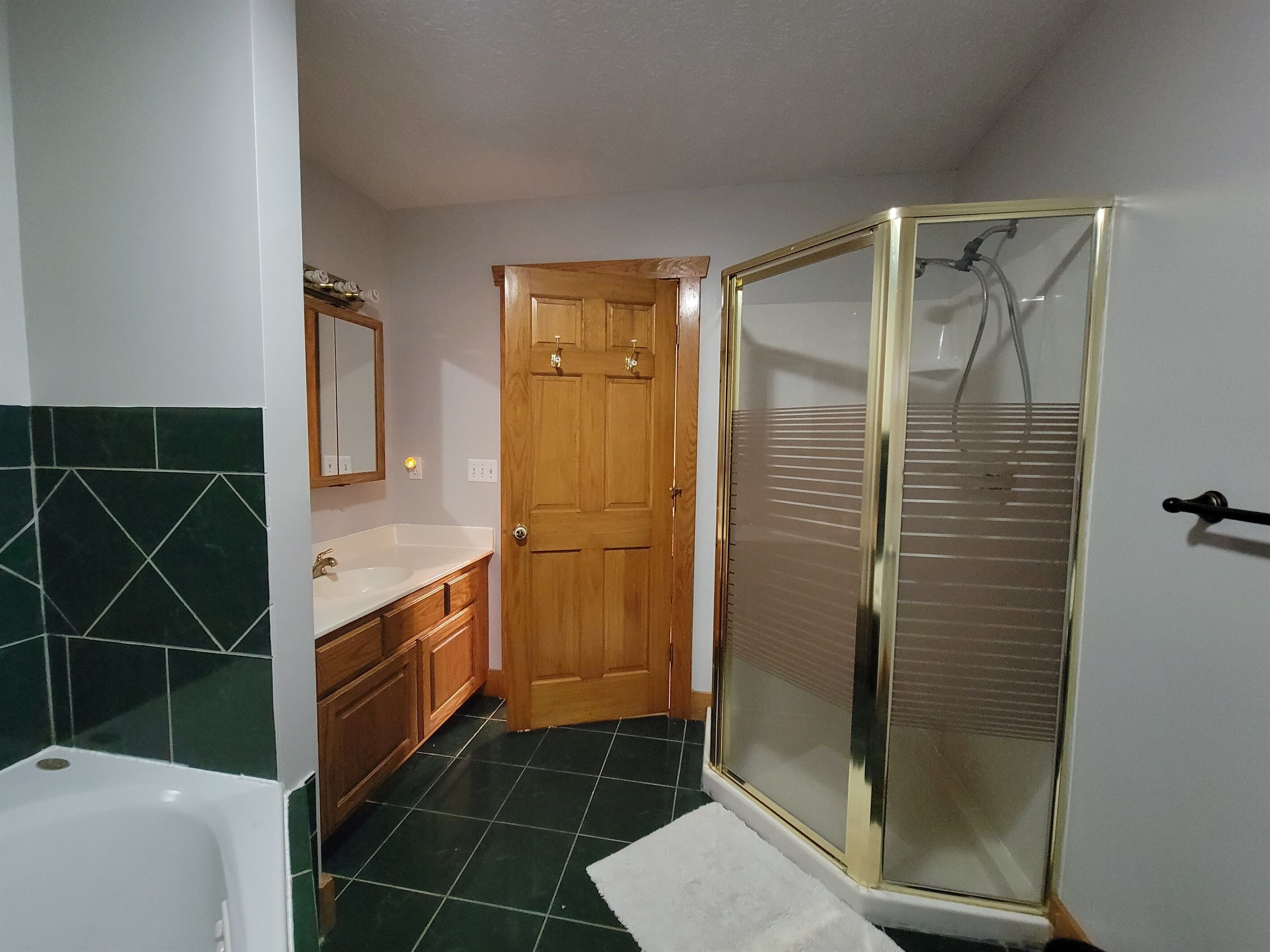 Ein Badezimmer mit einer Badewanne, einer Holztür, einer Duschkabine mit Glastüren und grünen Fliesen.