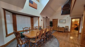 A dining area with a wooden table and chairs, a flag on the wall, and a staircase leading to an upper level.