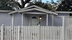 Un piccolo edificio a un piano con un recinto in legno bianco, una porta d'ingresso con un vetro e un piccolo portico.