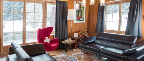 Ein gemütliches Wohnzimmer mit einem schwarzen Ledersofa, einem roten Sessel und einem Glastisch.