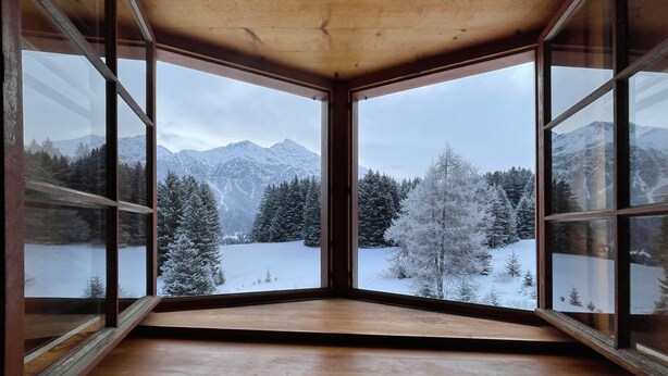 Habitación con amplios ventanales que ofrecen vistas a montañas nevadas y árboles.