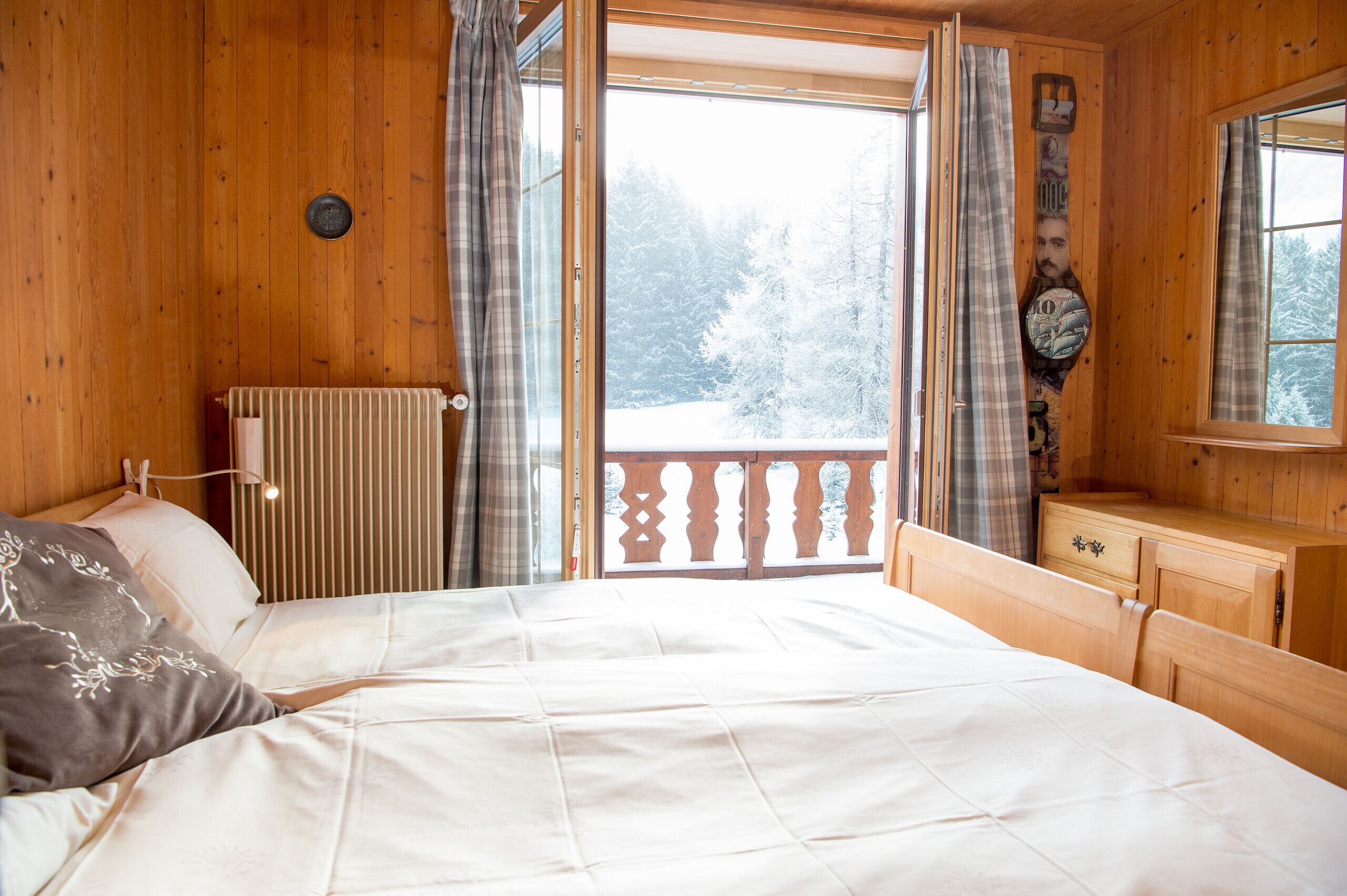 Une chambre à coucher dans une cabane en bois, avec un lit, une commode et une vue sur une forêt enneigée par une grande fenêtre.