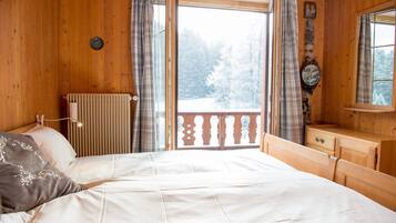 Une chambre à coucher dans une cabane en bois, avec un lit, une commode et une vue sur une forêt enneigée par une grande fenêtre.