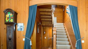 Una escalera de madera con un rellano alfombrado, flanqueado por cortinas azules, que conduce a una puerta.