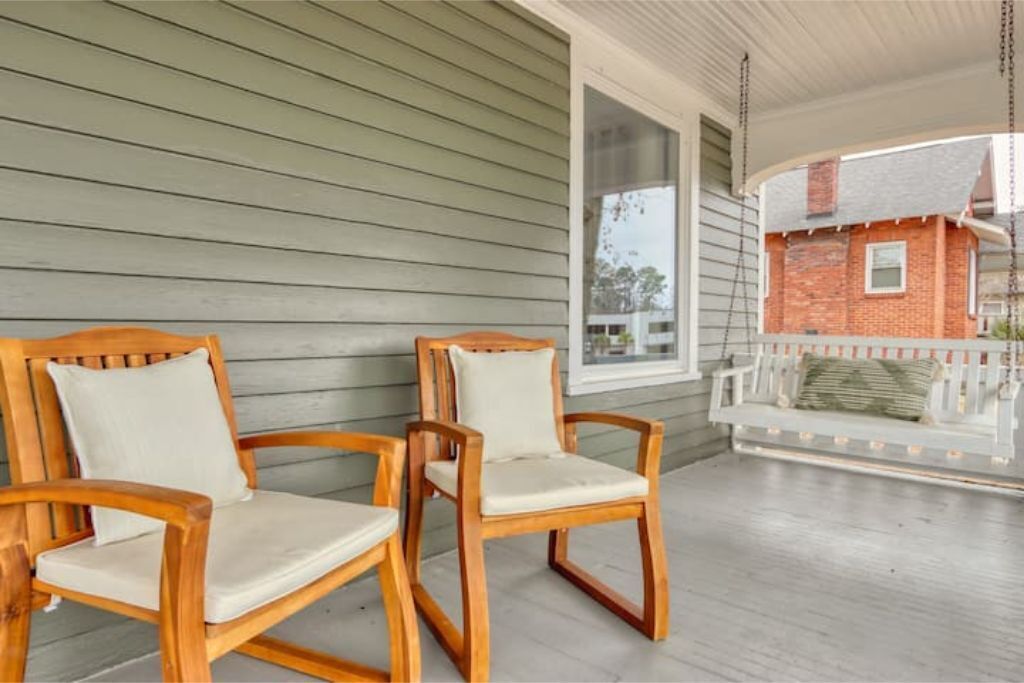 A porch with two wooden chairs and a white cushioned bench.