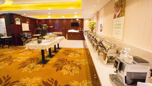A hotel conference room with tables, chairs, a coffee station, and a television on the wall.