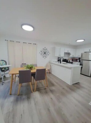 A modern kitchen with white cabinets, a central island, and a dining area with a table and chairs.
