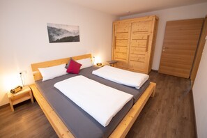 Une pièce comprenant un lit en bois, une table de chevet, un banc, une armoire et un tableau accroché au mur.