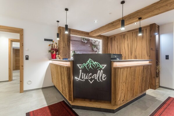 Un comptoir d’accueil avec un revêtement en bois et un panneau lumineux au néon sur lequel on peut lire « Luisalle ».