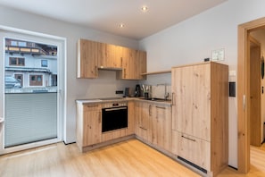 A modern kitchen with wooden cabinets, a built-in oven, and a large window overlooking a residential area.