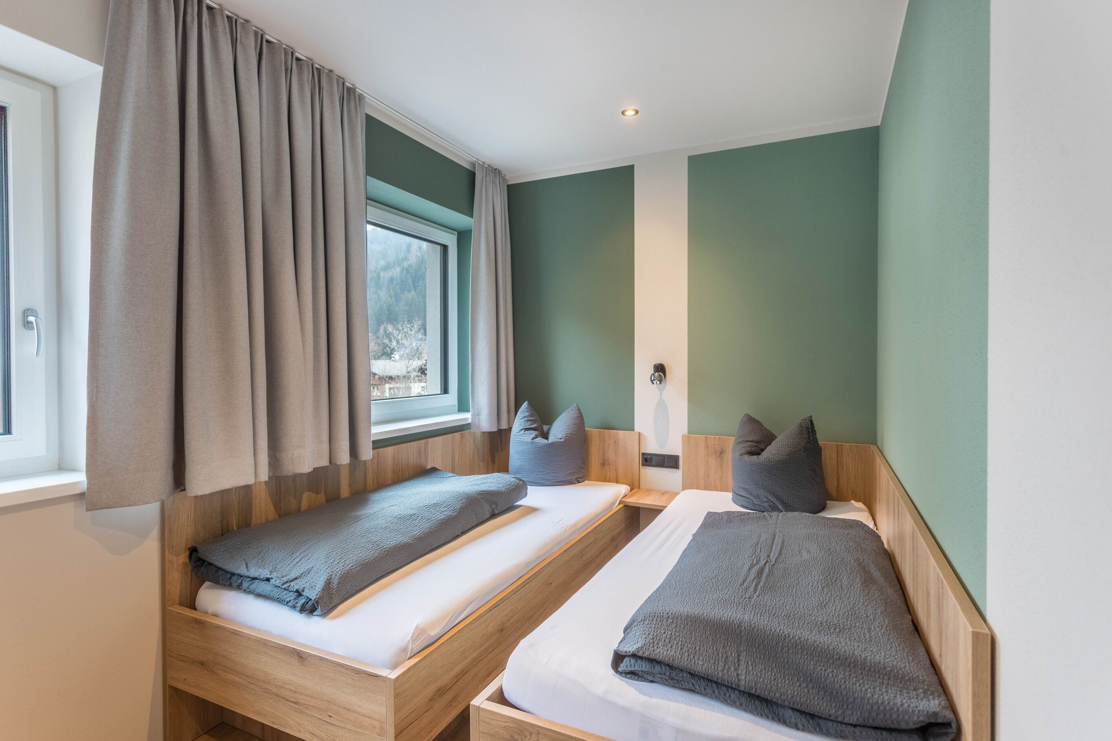 A room with two wooden beds, a window with curtains, and a wall-mounted light fixture.