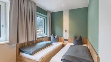A room with two wooden beds, a window with curtains, and a wall-mounted light fixture.