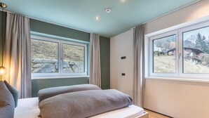Ein Schlafzimmer mit einem Bett, zwei Kissen, einem Nachttisch, einem Fenster mit Vorhängen und Blick auf einen Hügel.