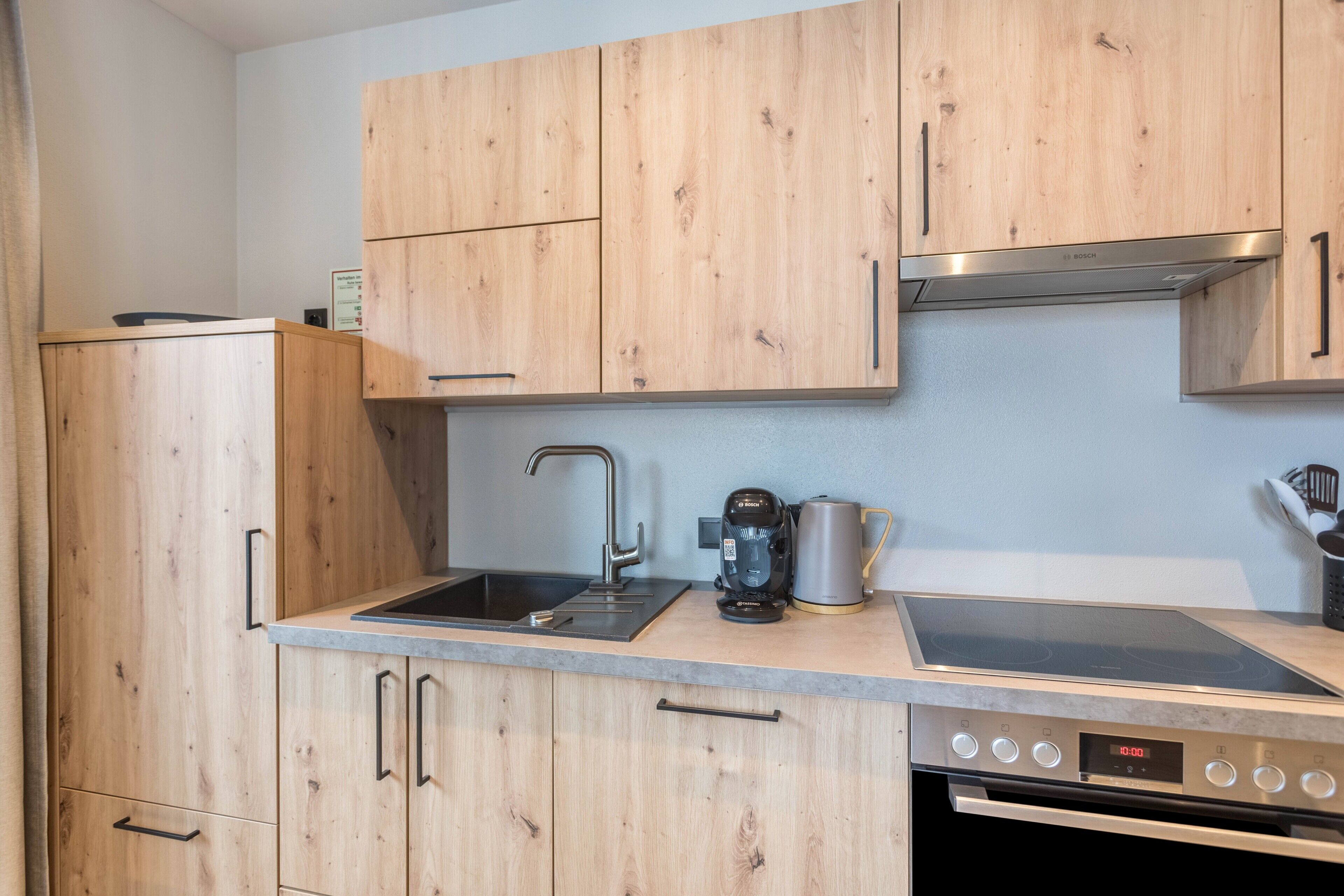 A kitchen with wooden cabinets, a sink, a coffee maker, and an oven.