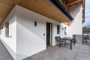 Un bâtiment moderne à l’extérieur blanc, doté d’un plafond en bois et d’un patio aménagé avec une table et des chaises.