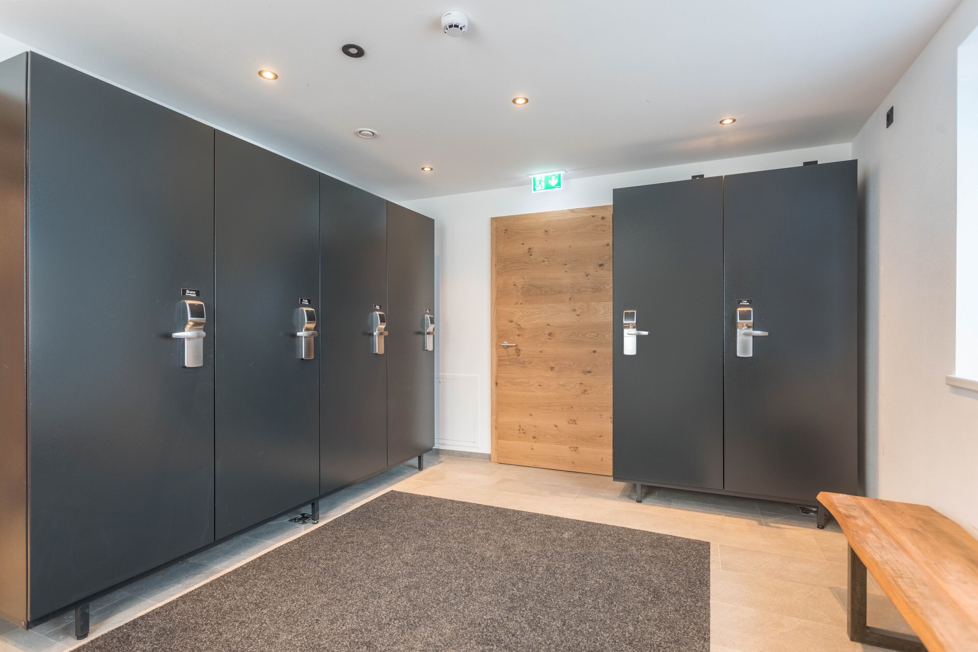 Een moderne hotelkamer met donkere kastjes, een houten deur, een bankje en een vloerbedekking.