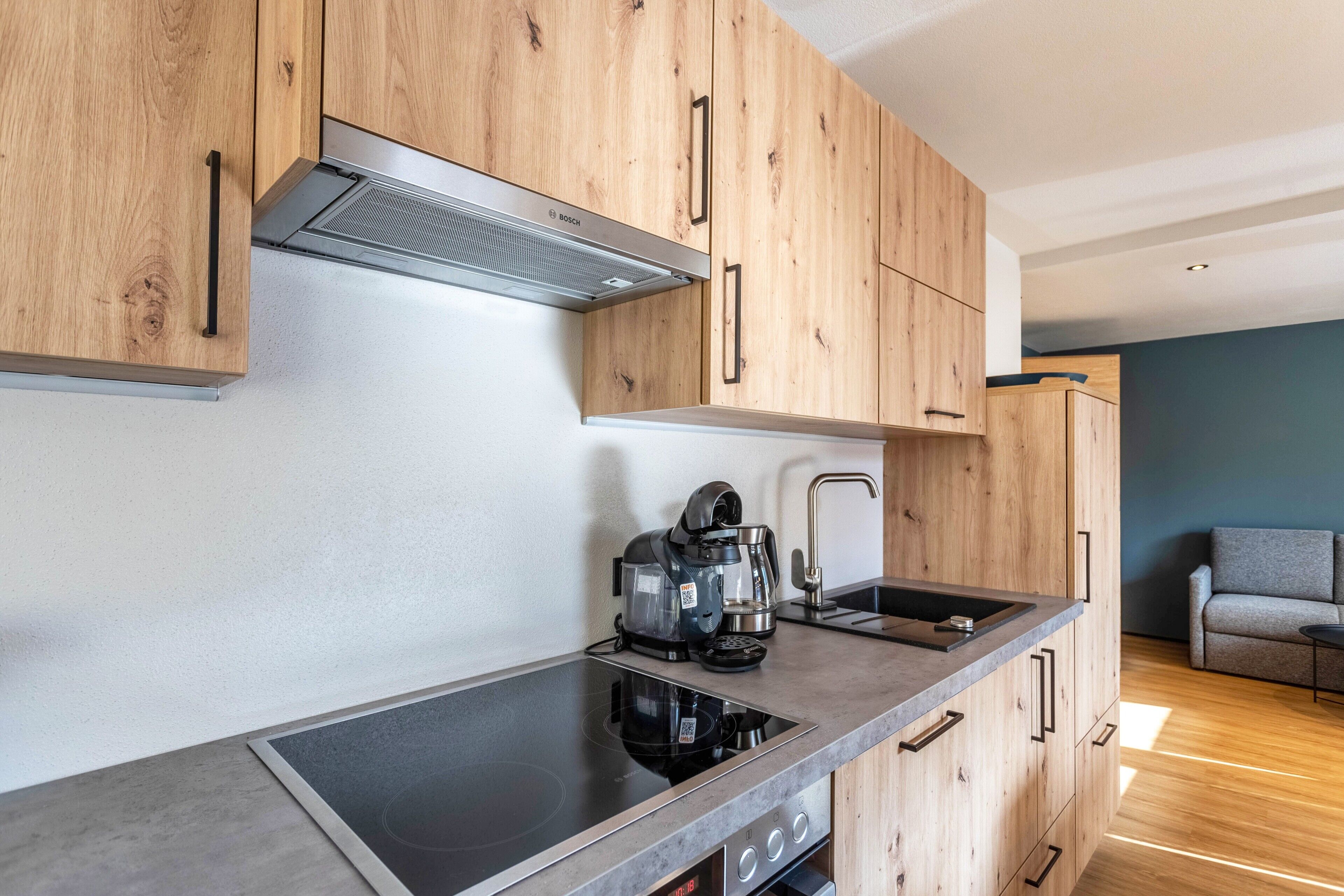 A modern kitchen with wooden cabinets, a Bosch range hood, a coffee maker, and a built-in induction cooktop.