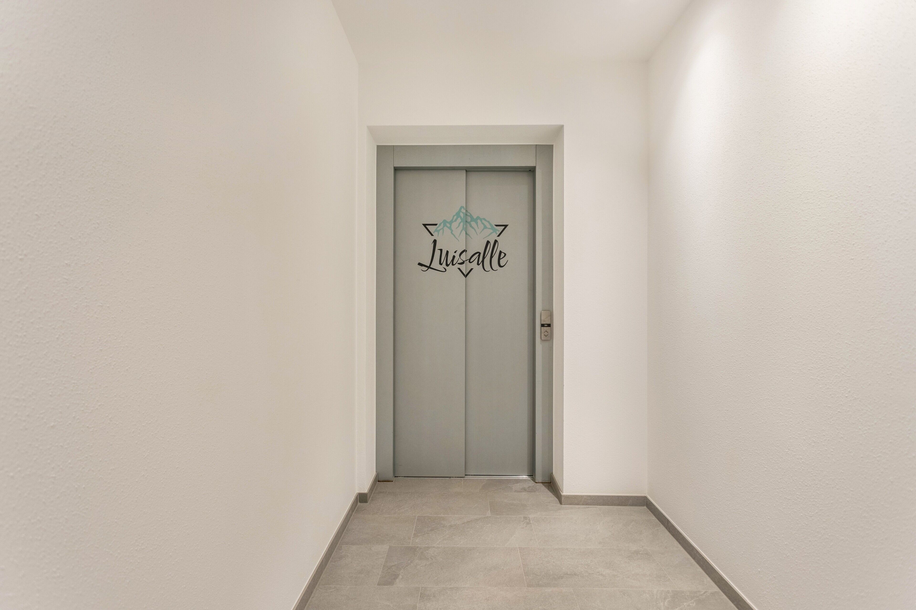 A hallway with a grey door featuring a mountain design and the name 'Luisalle' on it.