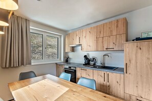 Una cocina moderna con armarios de madera, horno empotrado, lavamanos y comedor con mesa y sillas.
