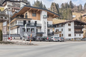 Un hotel de varios pisos con un cartel llamativo que dice 'Luisa', un estacionamiento con varios coches y un paisaje montañoso al fondo.