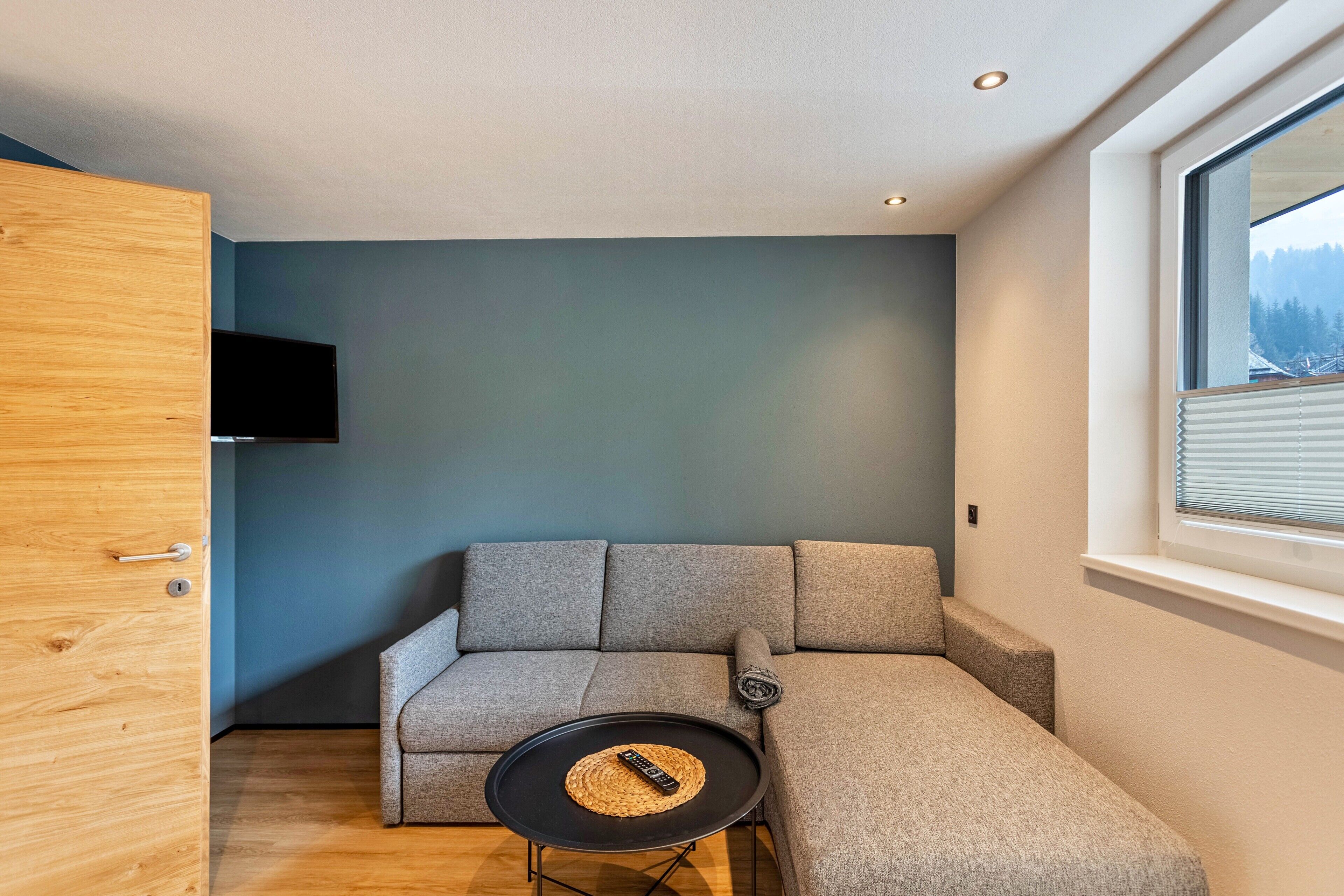 Un salon moderne avec un canapé d’angle, une petite table ronde et un téléviseur fixé au mur.