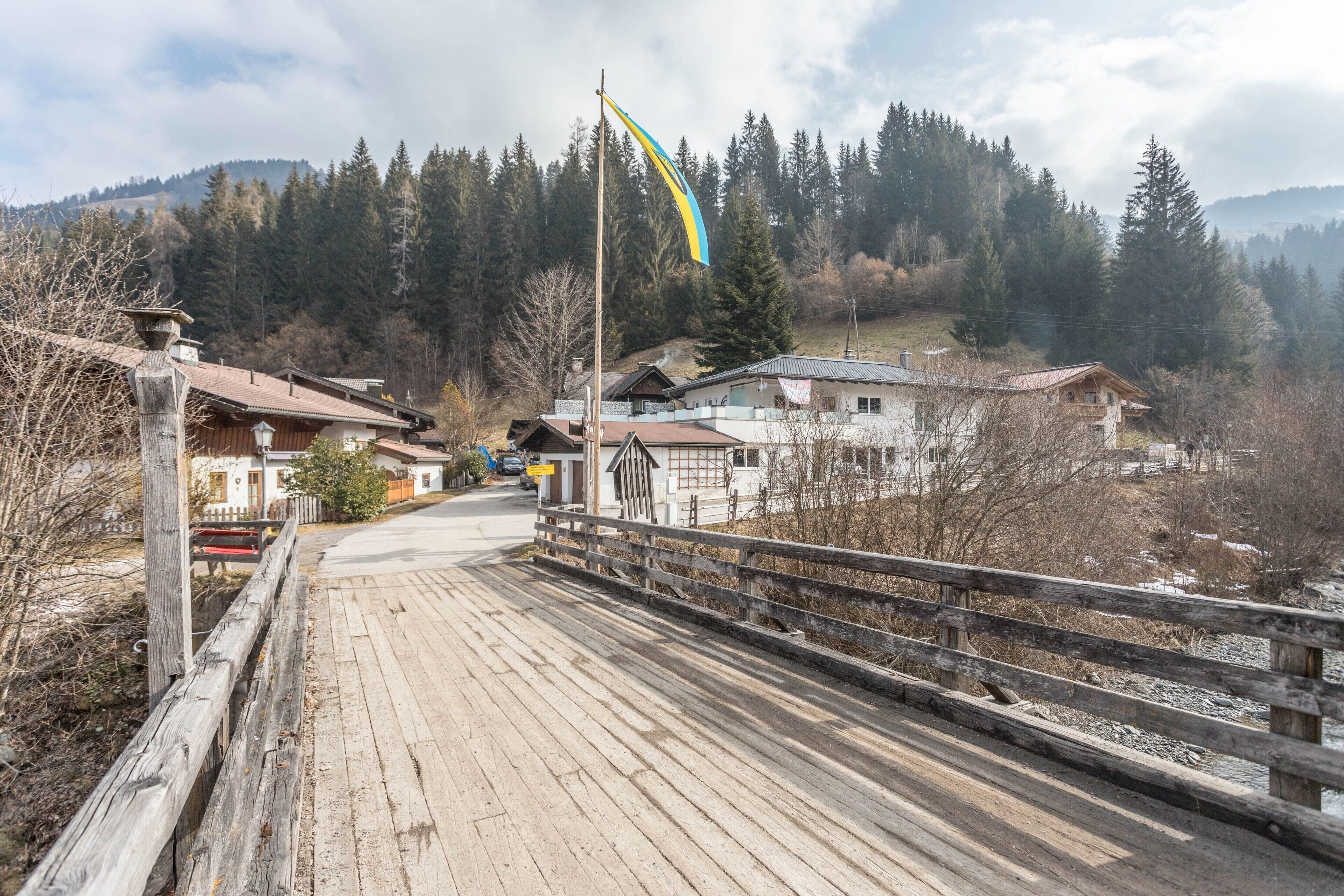 Eine Holzbrücke führt zu einer Reihe von Häusern, im Hintergrund weht eine Flagge.