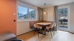 A dining area with a wooden table and chairs, a bench, and a view of a forest through large windows. - Apartment 'Luisalle Top 6' with Mountain View, Balcony and Wi-Fi (Auffach)