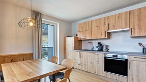 A modern kitchen with wooden cabinets, a built-in oven, and a dining area with a wooden table and chairs. - Apartment 'Luisalle Top 6' with Mountain View, Balcony and Wi-Fi (Auffach)