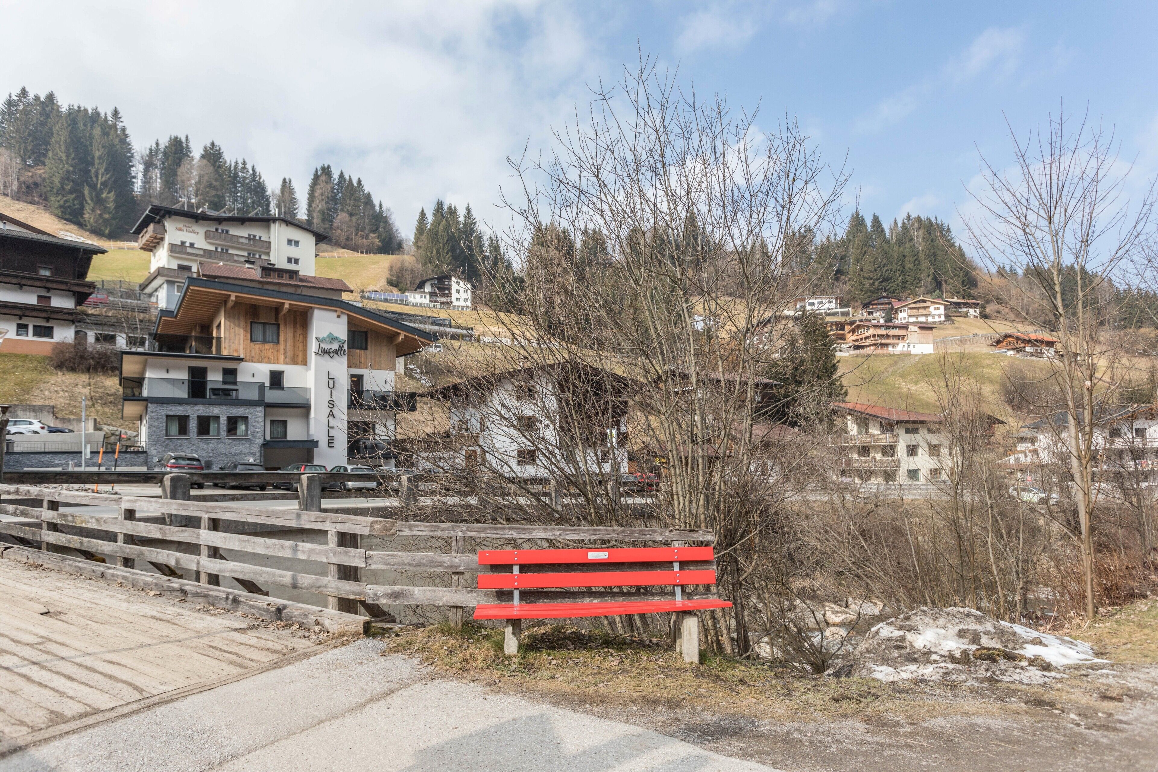 Un bâtiment sur lequel est affiché un panneau indiquant une vente, un banc rouge et une vue sur une zone vallonnée avec des arbres et d’autres bâtiments.