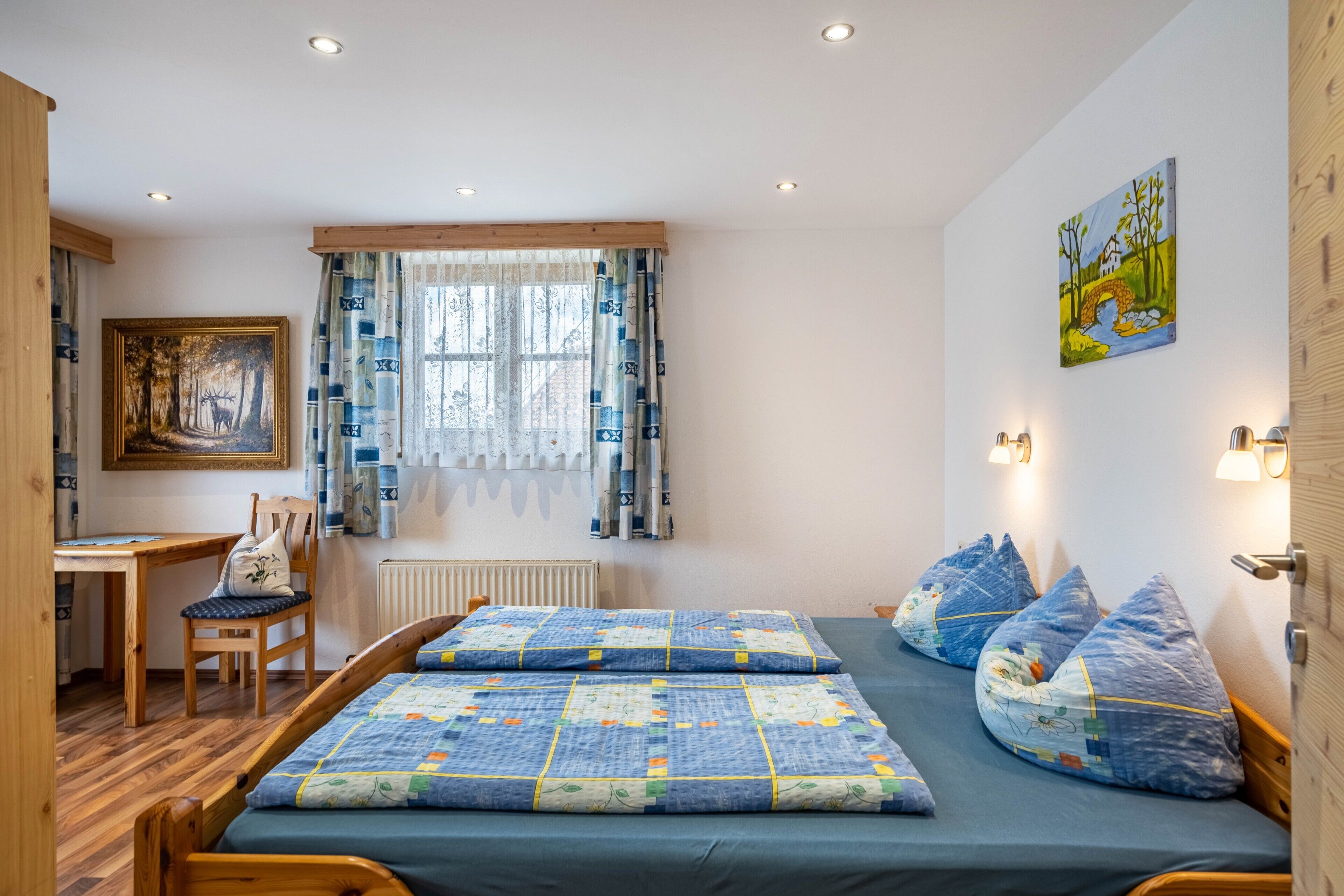 A bedroom with a bed, a desk, a chair, a window with curtains, and a painting on the wall.