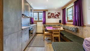A compact kitchen with modern appliances, a dining area with a bench, and large windows with purple curtains. - Apartment 'Unterlehenhof A' with Mountain View, Balcony and Wi-Fi (Zell am Ziller)