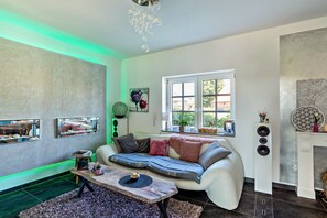 Una sala de estar moderna con un sofá modular, una mesa de centro, un ventanal grande y una lámpara de techo decorativa.