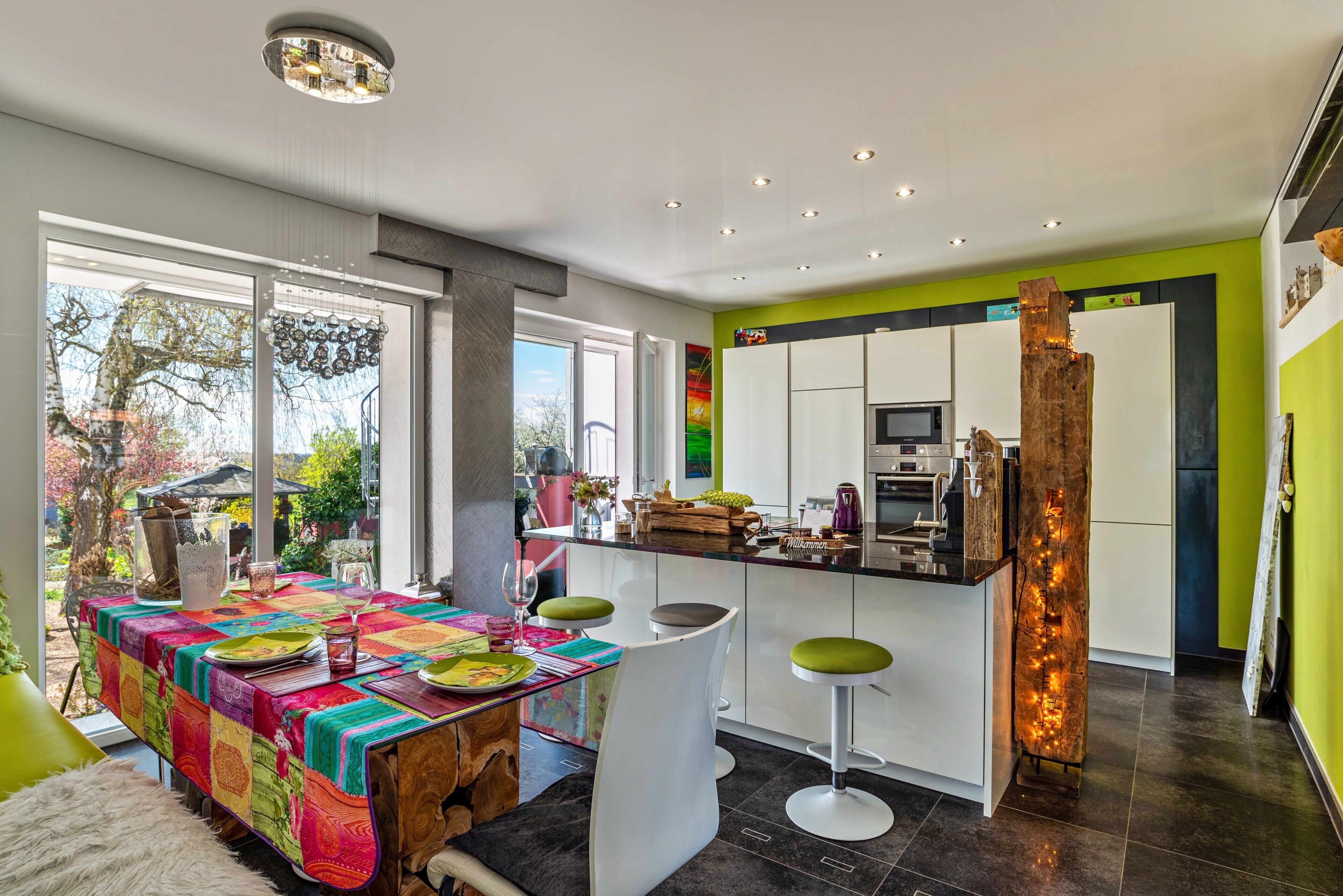 A modern kitchen with a central island, bar stools, and a dining area with a colorful tablecloth.
